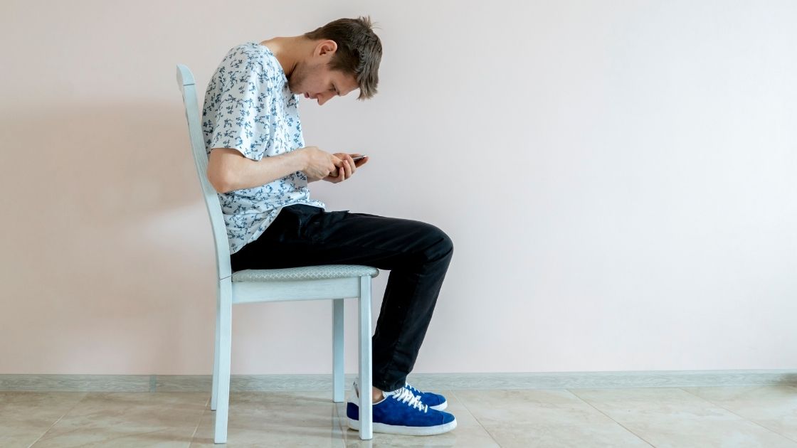 person sitting hunched over on a chair with bad posture looking at phone