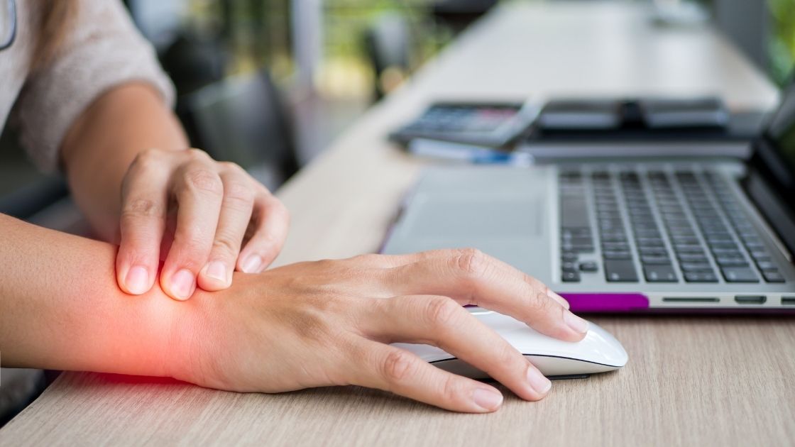 person grabbing wrist at desk with wrist pain with a computer mouse in their hand