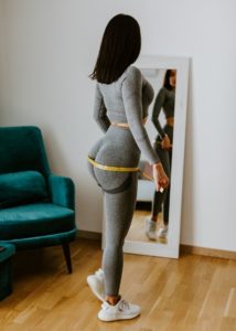 woman measuring her butt with a tape measure standing in front of a mirror