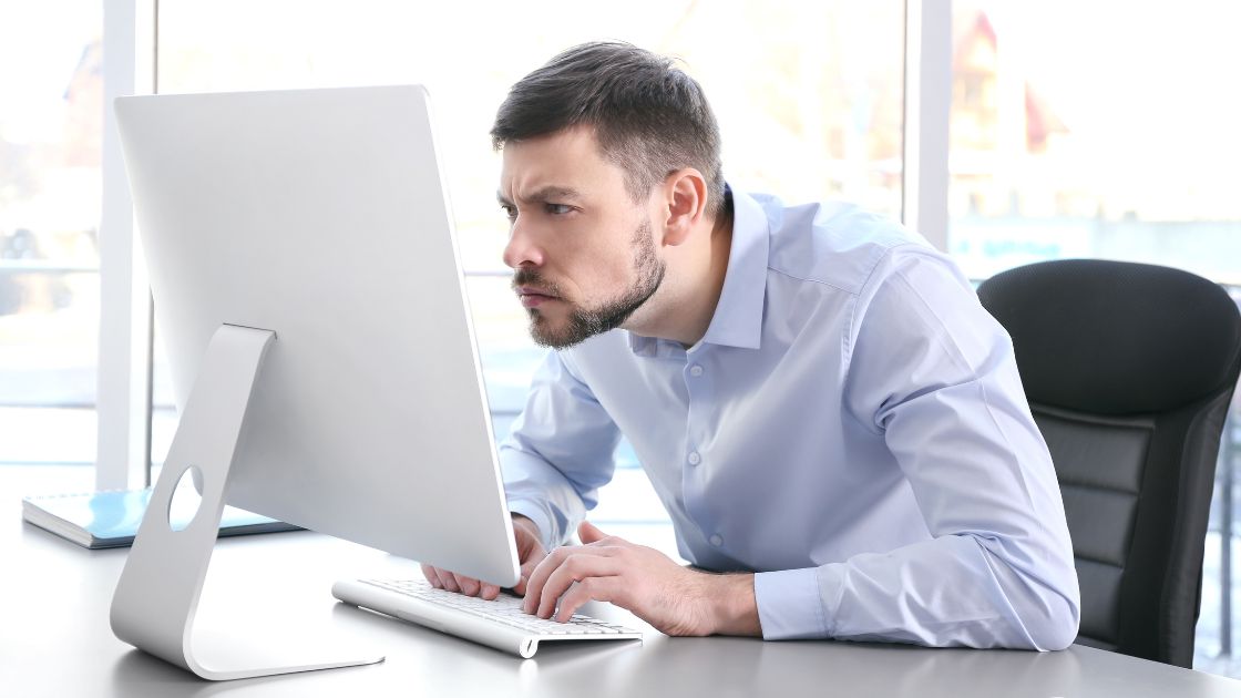 man hunched over at desk looking at computer monitor