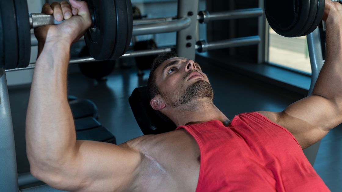 man in a red top doing a bench press with dumbbells
