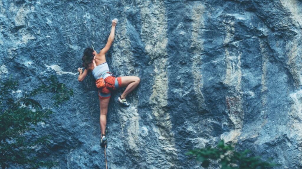 woman rock climbing reaching up with right arm