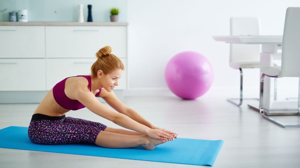 woman in purple sitting on a blue yoga mat in a pike stretch to stretch out the calves and back of the legs