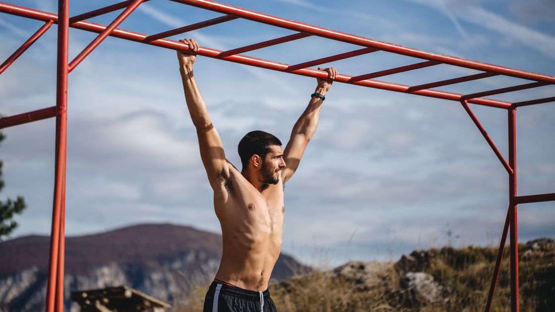 man hanging from monkey bars outside without a shirt on