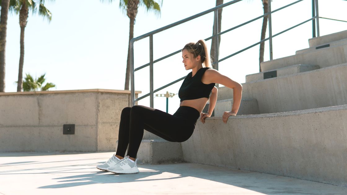 woman in black clothes doing triceps dips outside on cement stairs