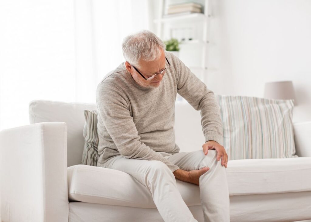 senior elderly man sitting on sofa with knee pain