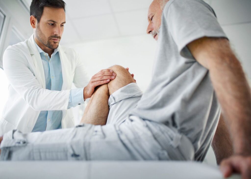 doctor examining elderly man's knee pain