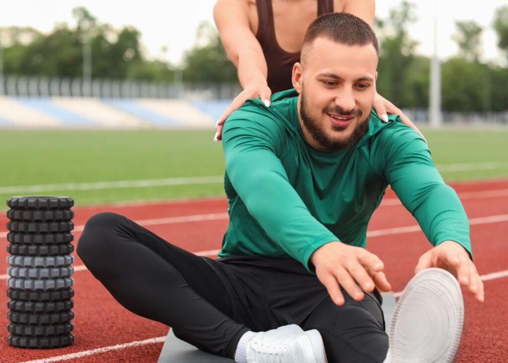 man stretching outside with female trainer