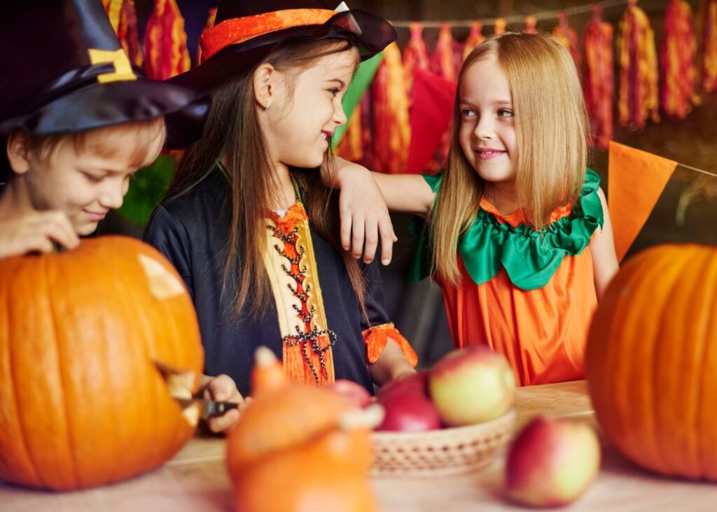kids dressed up in witch and pumpkin costumes while carving a pumpkin