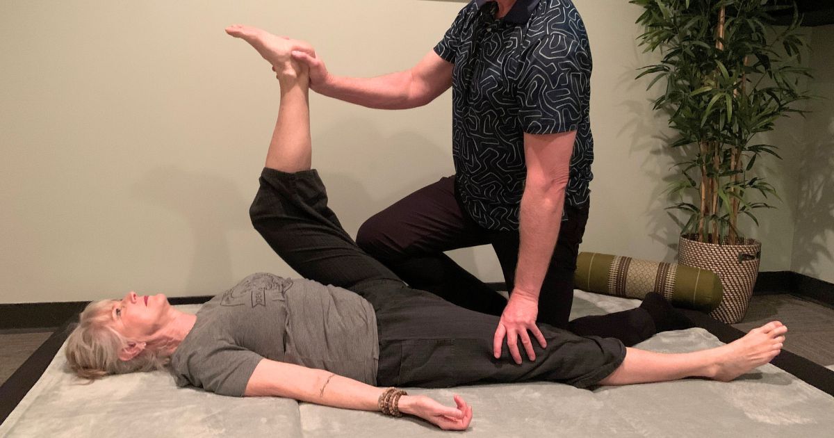 woman having leg stretched on floor during zen fusion massage
