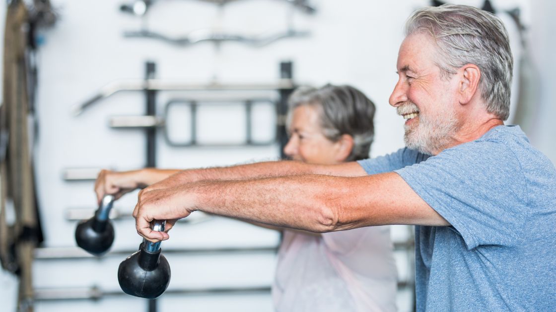 couple in their 60's working out together doing dumbbell forward lifts