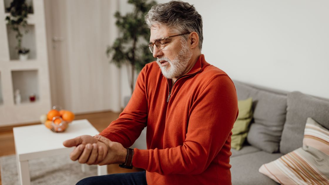 man in orange shirt holding wrist due to muscle stiffness