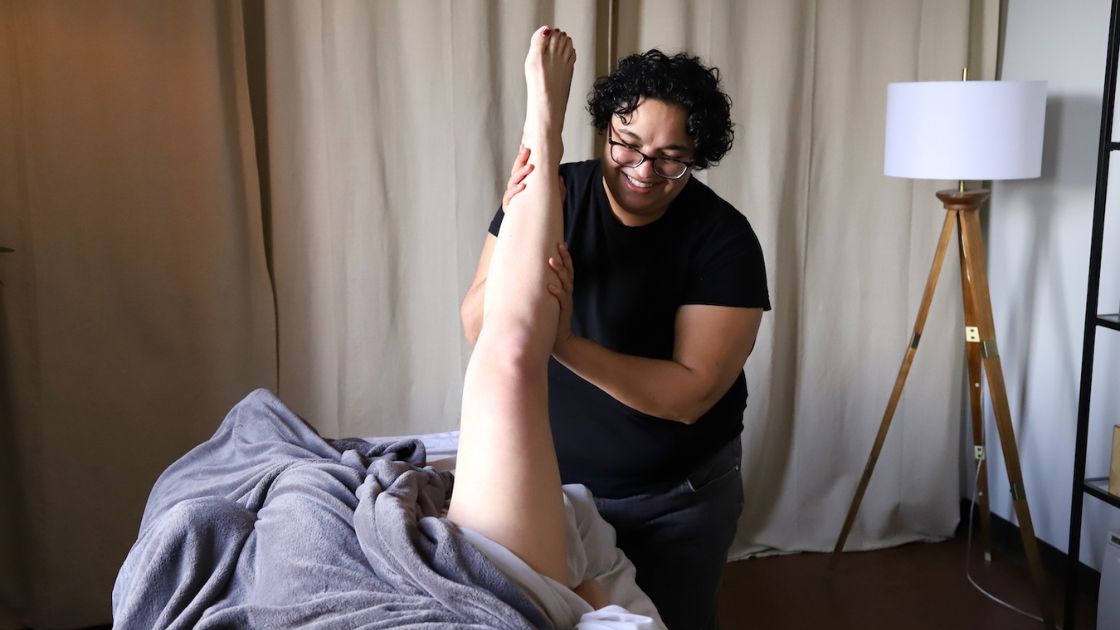massage therapist giving patient a sports massage on leg lifted in the air