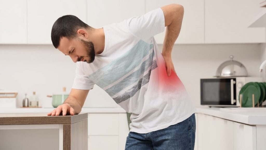 Man grabbing back in pain while stood in the kitchen