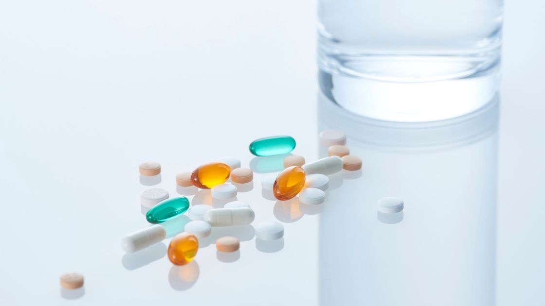 pills sitting next to a glass of water on a white counter